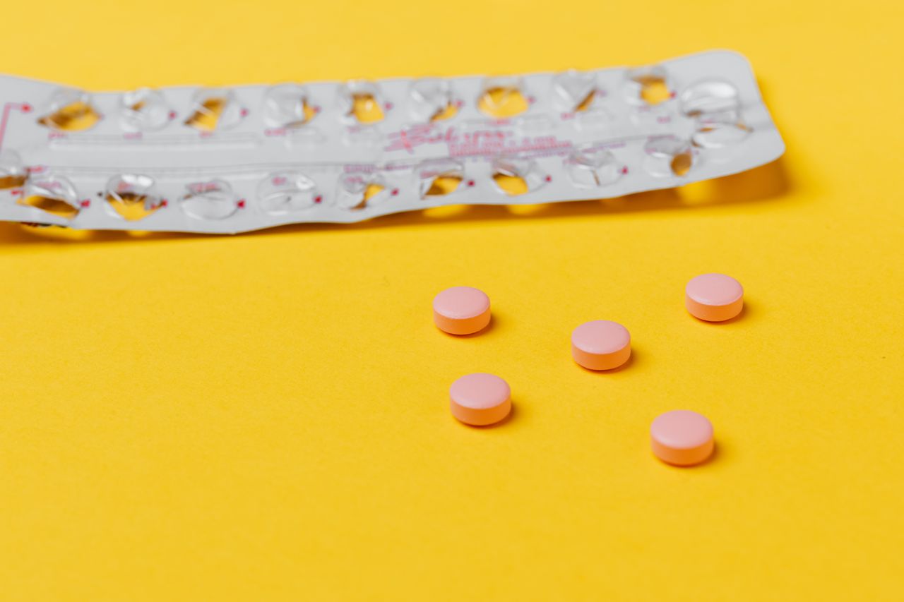 Services Pink pills and empty blister pack on a vibrant yellow surface.