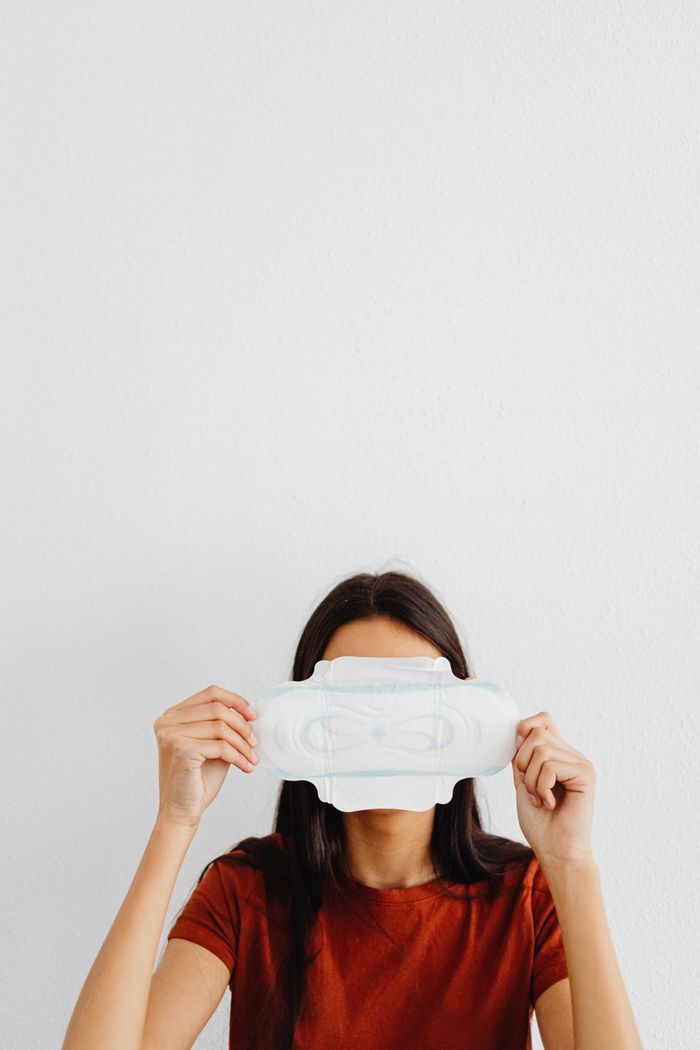 About A woman holds a sanitary pad in front of her face against a minimalist background.