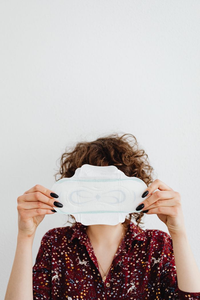 Services A woman is holding a sanitary pad in front of a white background, highlighting feminine hygiene products.